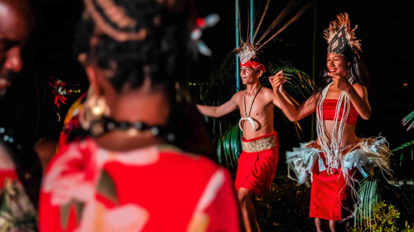 Two dancers in red costumes extend their arms onstage