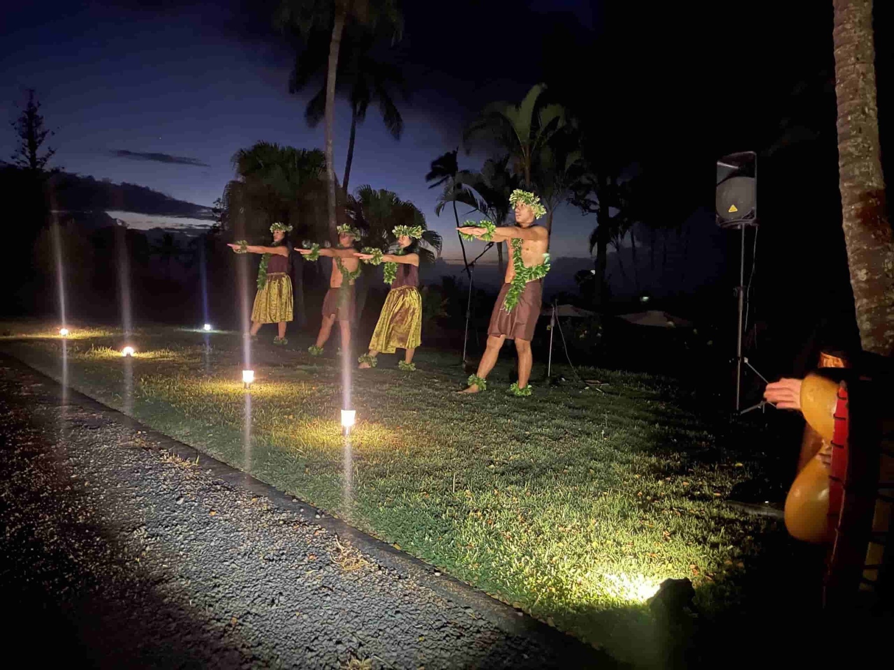 Hula dancers performing together on a lawn at dusk