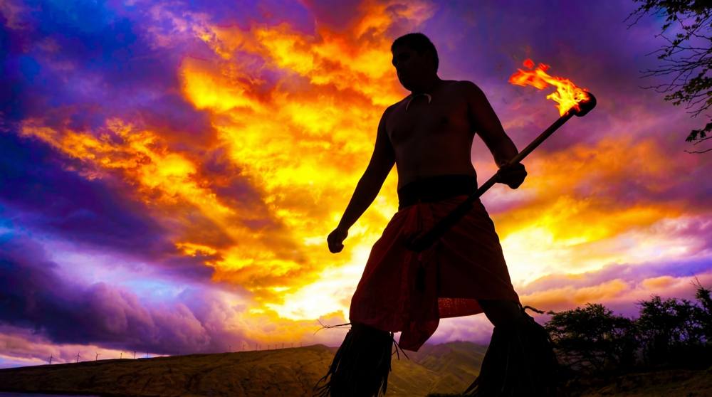 Fire knife dancer silhouetted against a vivid sunset