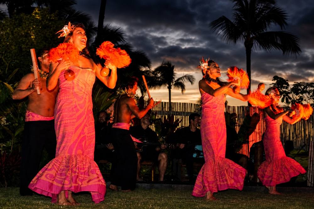 Tahitian dancers in orange costumes performing at dusk