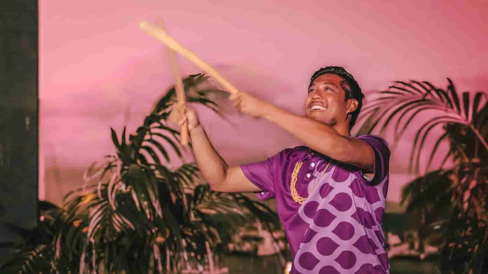Male performer joyfully throwing baton against pink evening sky