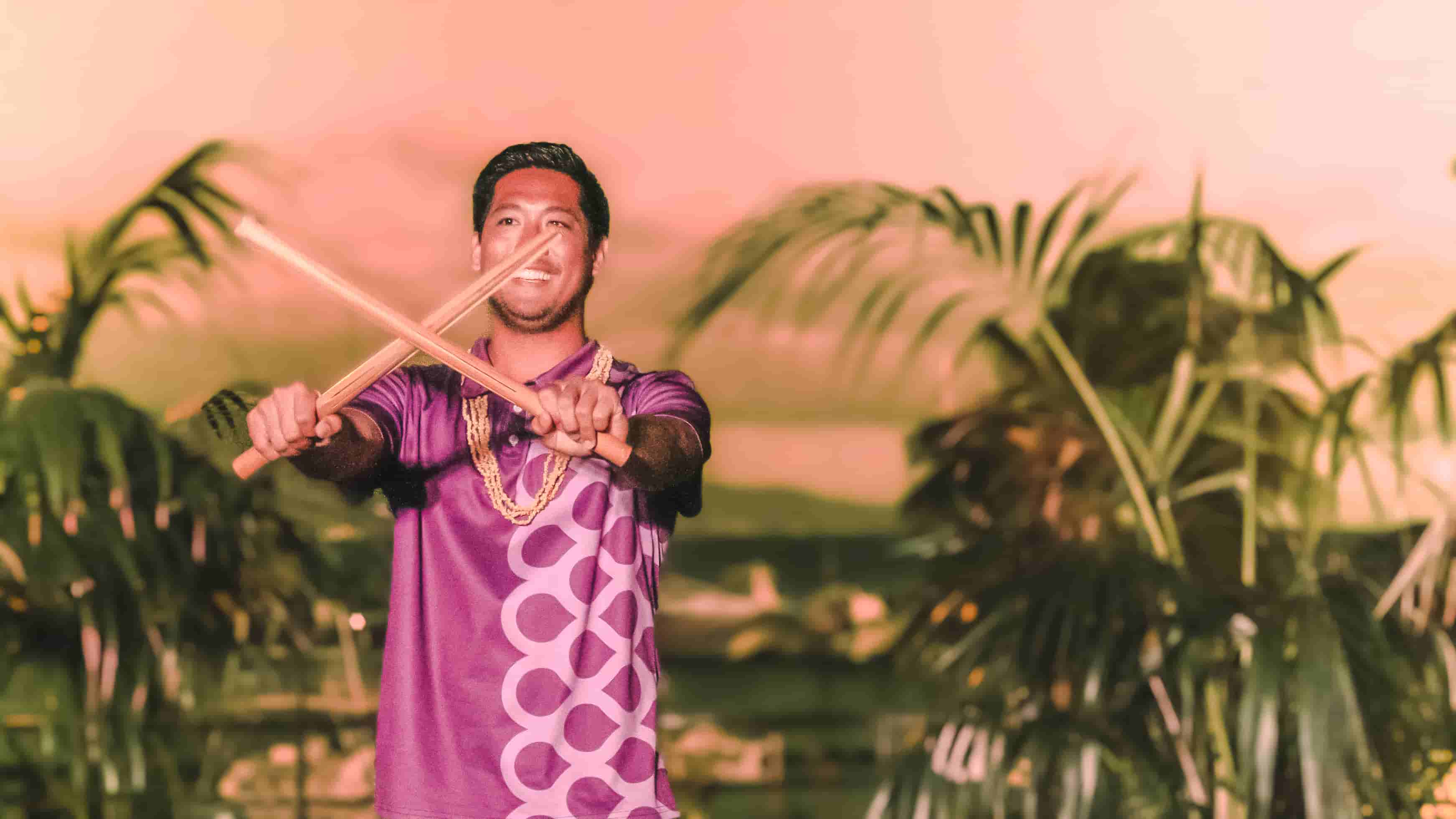 Male Polynesian performer with fire batons against pink sunset sky