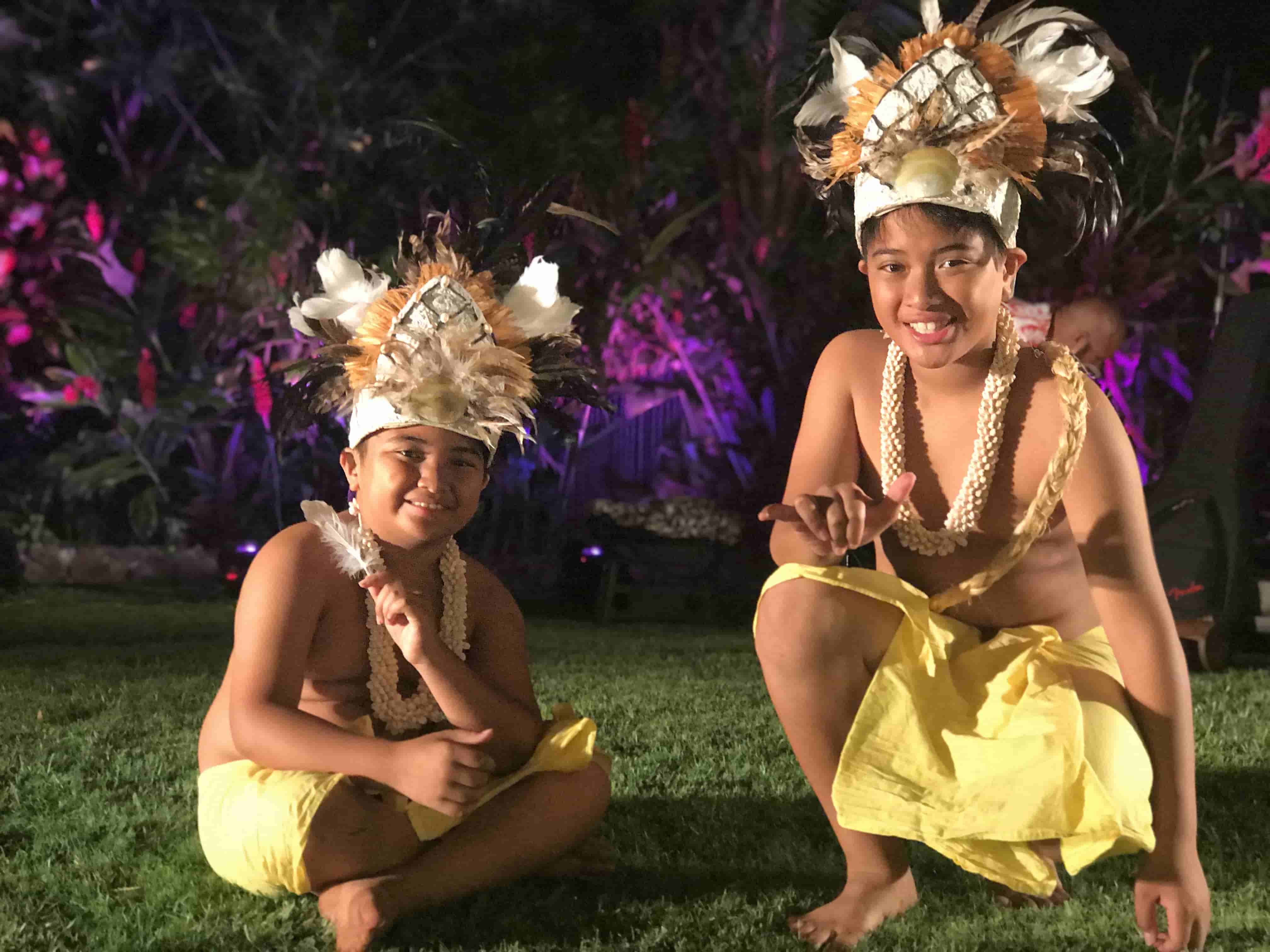 Two young children in traditional headdresses performing under purple lights